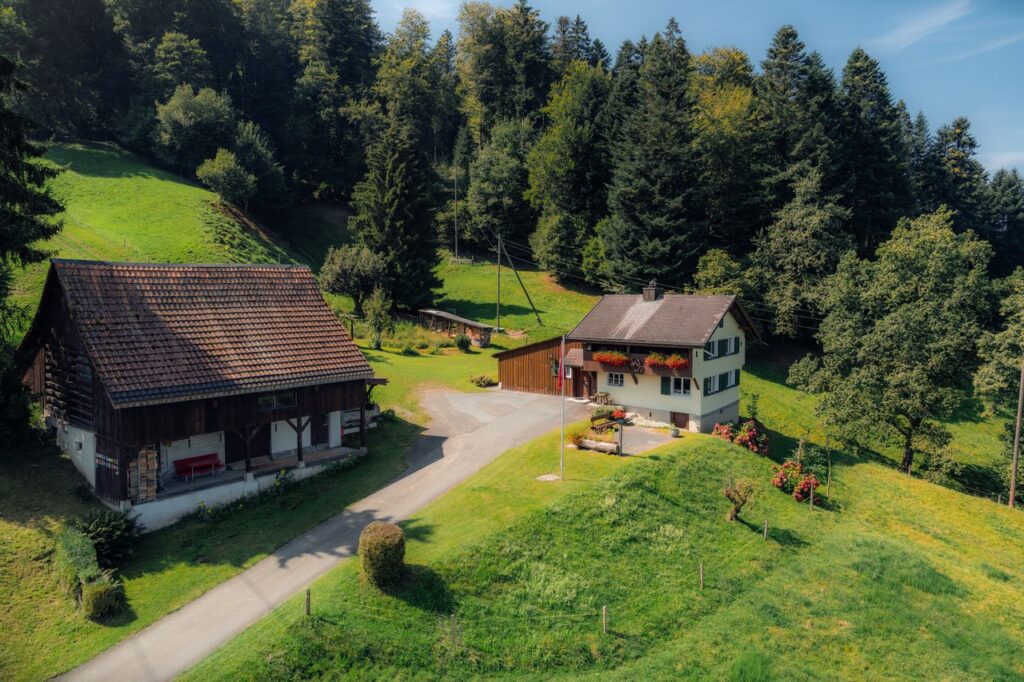 Netzwerk A stunning aerial view capturing a rural farmhouse surrounded by lush greenery and a dense forest, showcasing the beauty of nature.
